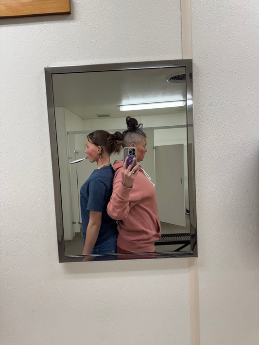 two tall women standing back to back comparing height in the reflection in a mirror